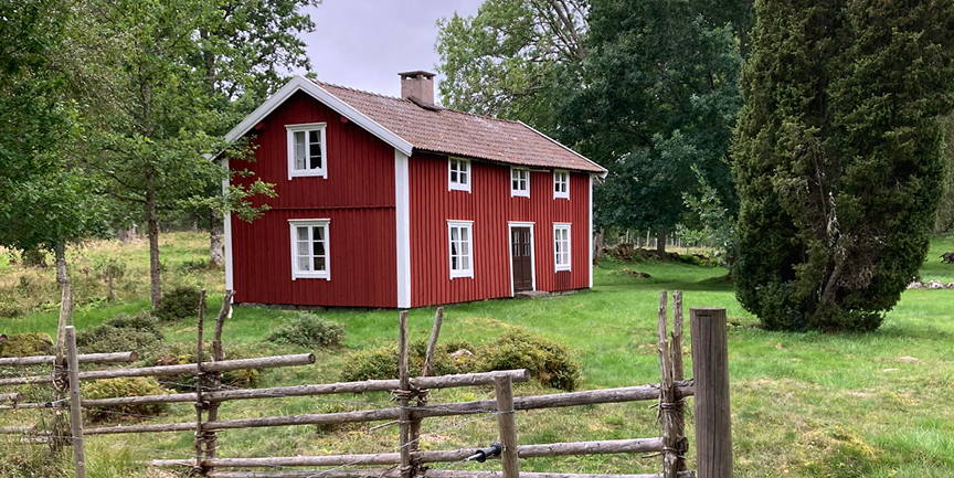 En röd stuga med gärdsgårdsstaket framför