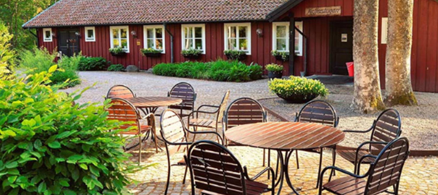 Utanför Kaffestugan i Apladalen med utemöbler och den röda stugan i bakgrunden.